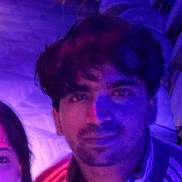 Close-up of a man with dark hair bathed in dramatic purple and blue neon light.