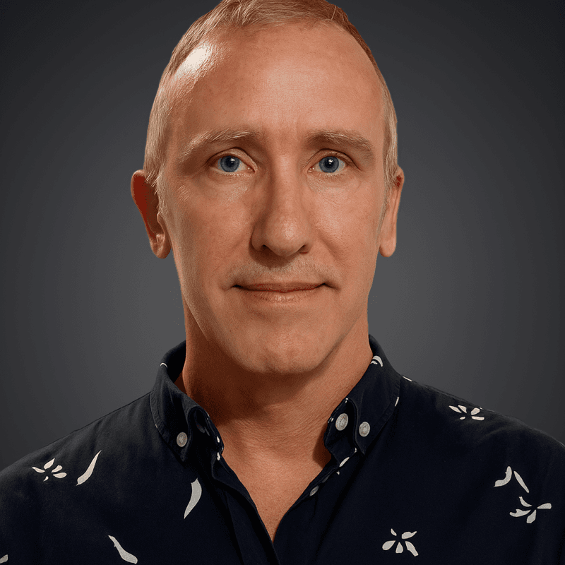 Middle-aged man with short light hair and blue eyes wearing a navy patterned shirt.