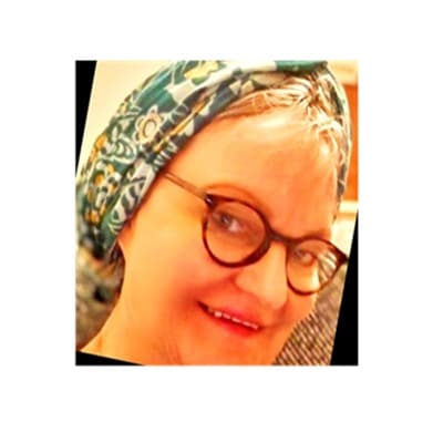 Smiling woman wearing round glasses and a green and yellow patterned headscarf.